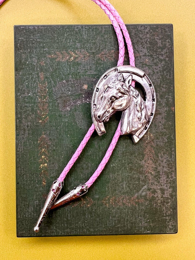 Bolo tie with horse head design on a pink cord against a yellow background