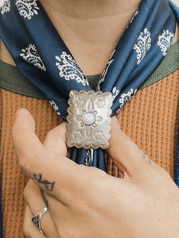 Person adjusting a patterned scarf around their neck with a blue coat and brown shirt.